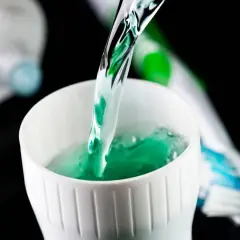 Enjuague bucal verde vertiéndose en un vaso blanco, parte de la rutina de fluorización dental en adultos.