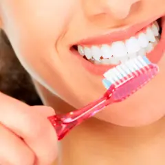 Una mujer se cepilla los dientes con una sonrisa radiante. Con un cepillado diario, se puede quitar una caries y mantener una boca sana.
