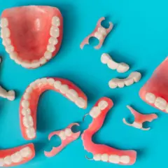 Variedad de protesicos dentales, incluyendo dentaduras completas y parciales, esparcidos sobre un fondo azul.