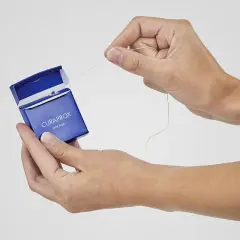 Manos sacando hilo dental de caja azul Curaprox. ¿El hilo dental se pasa antes o después del cepillado?