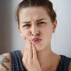 Mujer con expresión de dolor, tocándose la mejilla, posible hematoma por implante dental.