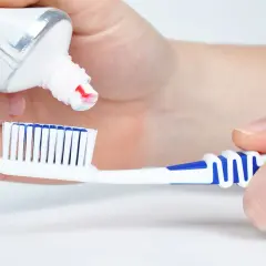 Manos aplican pasta de dientes a un cepillo. La pasta de dientes está hecha de ingredientes que limpian y protegen.