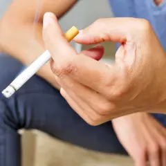 Mano sujetando un cigarrillo encendido. Fumar aumenta el riesgo de rechazo de implantes dentales.