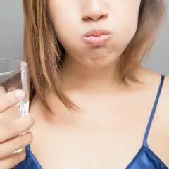 Mujer con la boca llena de agua, preparándose para enjuagarse después de lavarse los dientes.