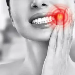 Mujer con dolor de muelas, señalando su mejilla donde se ve un **quiste en la encía** con un brillo rojo.