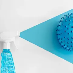 Botella rociadora con líquido azul y burbujas, apuntando a una esfera azul con púas. Considerar clorhexidina contraindicaciones.