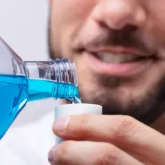 Hombre sonriente vierte clorhexidina diluida en un vasito dosificador para su higiene bucal.