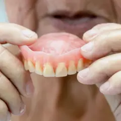 Manos de anciano sostienen una arcada dental superior, mostrando los dientes postizos.