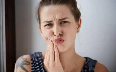 Mujer con expresión de dolor, tocándose la mejilla, posible hematoma por implante dental.