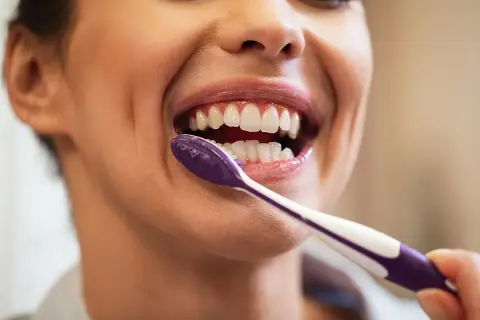 Primer plano de una mujer sonriendo mientras se lava los dientes con un cepillo morado.