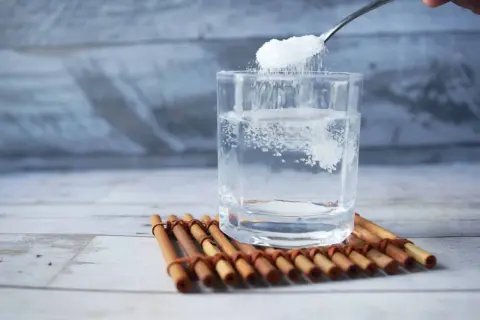 Cuchara añade sal a un vaso de agua, remedio casero para aliviar las encías inflamadas.