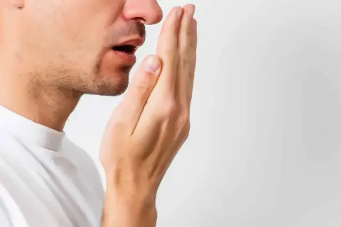 Hombre revisando su aliento, buscando soluciones para la halitosis.