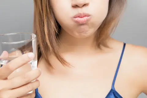 Mujer con la boca llena de agua, preparándose para enjuagarse después de lavarse los dientes.