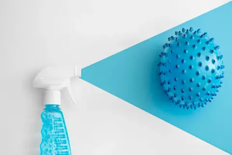 Botella rociadora con líquido azul y burbujas, apuntando a una esfera azul con púas. Considerar clorhexidina contraindicaciones.