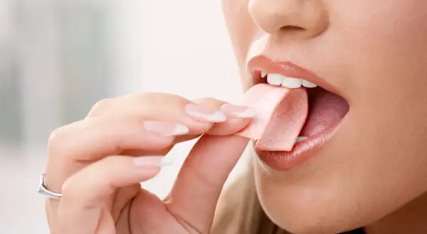 Una mujer se lleva un trozo de chicle a la boca para masticar chicle.