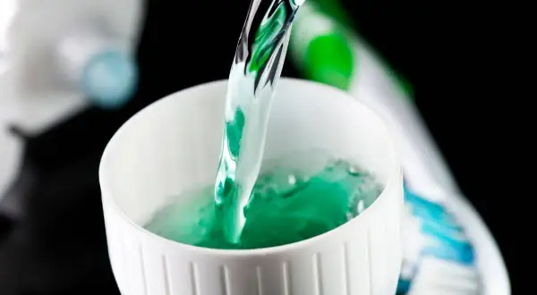 Enjuague bucal verde vertiéndose en un vaso blanco, parte de la rutina de fluorización dental en adultos.