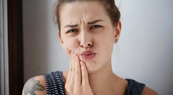 Mujer con expresión de dolor, tocándose la mejilla, posible hematoma por implante dental.