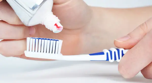 Manos aplican pasta de dientes a un cepillo. La pasta de dientes está hecha de ingredientes que limpian y protegen.