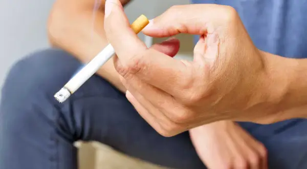 Mano sujetando un cigarrillo encendido. Fumar aumenta el riesgo de rechazo de implantes dentales.