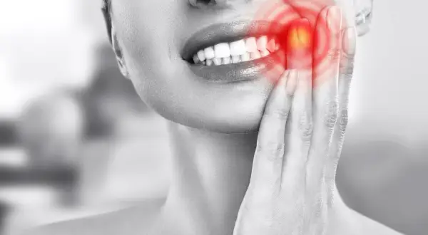Mujer con dolor de muelas, señalando su mejilla donde se ve un **quiste en la encía** con un brillo rojo.