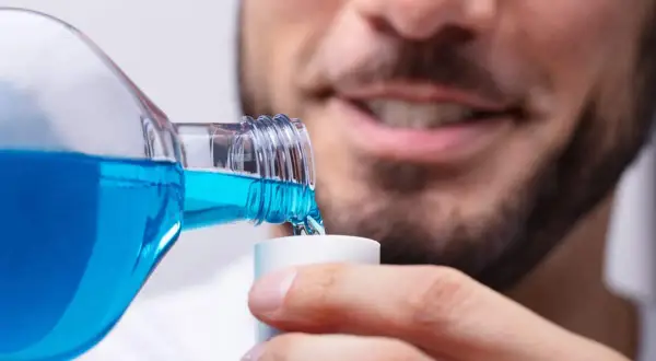 Hombre sonriente vierte clorhexidina diluida en un vasito dosificador para su higiene bucal.