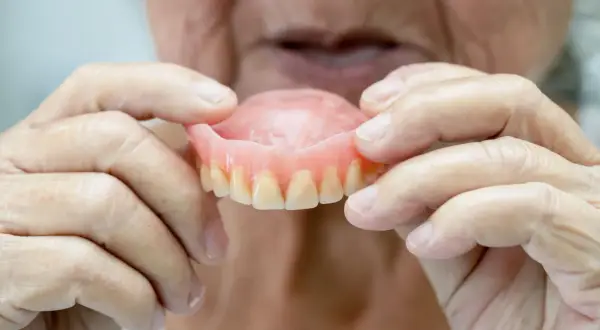Manos de anciano sostienen una arcada dental superior, mostrando los dientes postizos.