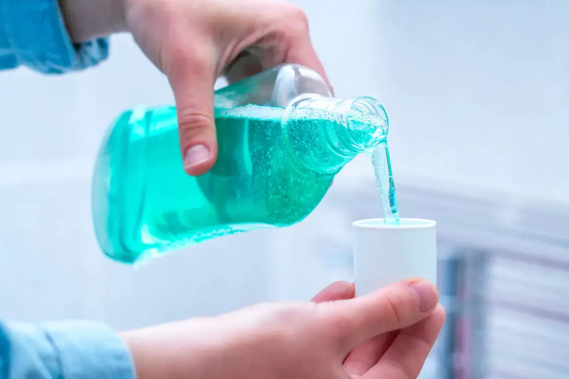 Mano vierte líquido azul de una botella a una taza medidora, mostrando varios tipos de clorhexidina para higiene bucal.