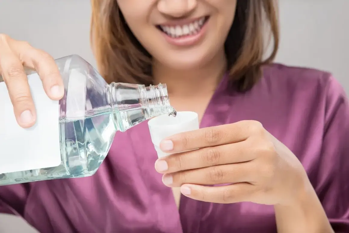 Mujer sonriente vierte líquido de una botella a una taza. Podría ser clorhexidina o agua con sal para enjuague bucal.