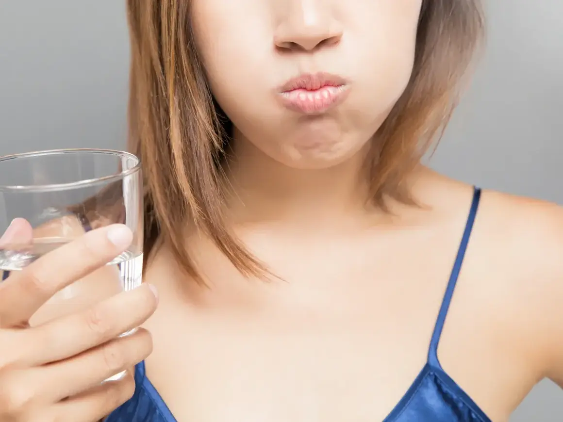 Mujer con la boca llena de agua, preparándose para enjuagarse después de lavarse los dientes.