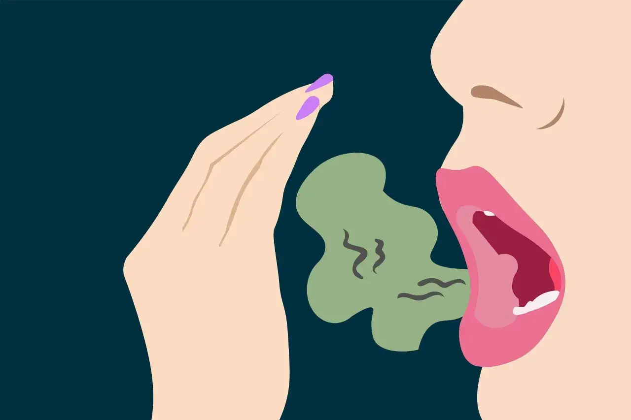 Una mano cubre la boca abierta de una persona, de la que emana una nube verde con rizos, indicando cómo saber si me huele el aliento.