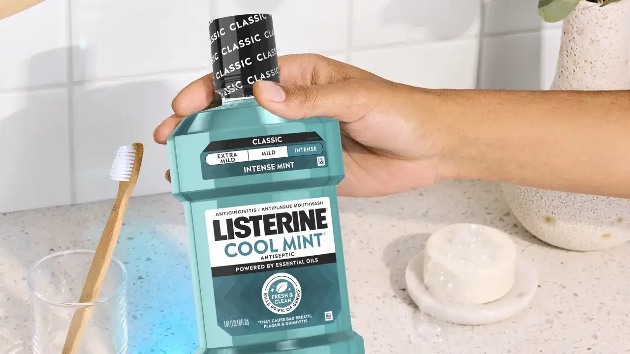 Mano sosteniendo Listerine Cool Mint. Un cepillo de dientes de bamb&uacute; y una pastilla de jab&oacute;n est&aacute;n cerca. Ideal para la higiene bucal y el cuidado de las mucosas.