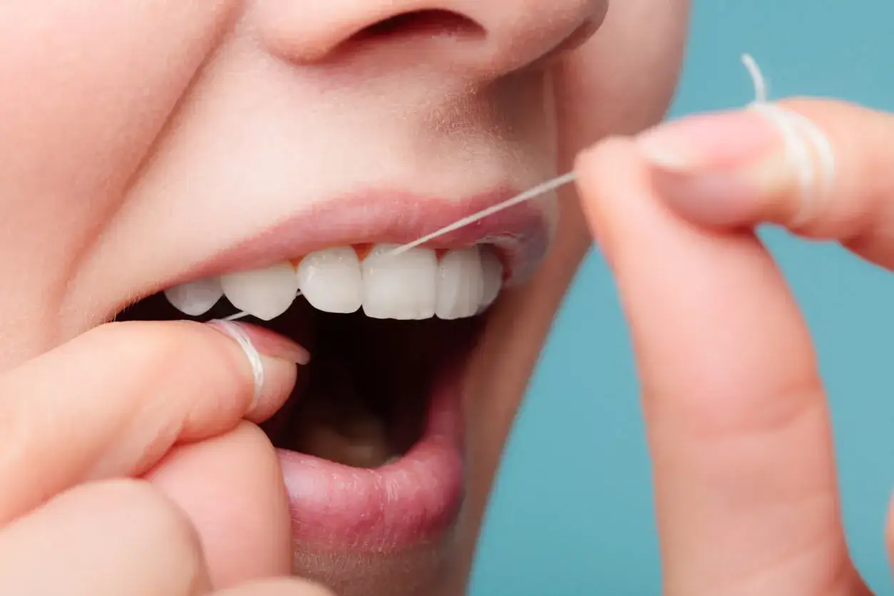 Persona usa hilo dental para limpiar sus dientes. El hilo dental sirve para eliminar restos de comida y placa bacteriana entre los dientes.