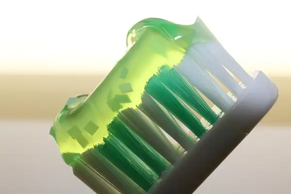 Cepillo de dientes con pasta verde, destacando los beneficios del fluor en los dientes para una sonrisa sana y protegida.