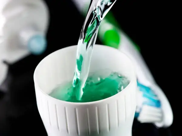 Enjuague bucal verde vertiéndose en un vaso blanco, parte de la rutina de fluorización dental en adultos.
