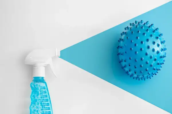 Botella rociadora con líquido azul y burbujas, apuntando a una esfera azul con púas. Considerar clorhexidina contraindicaciones.